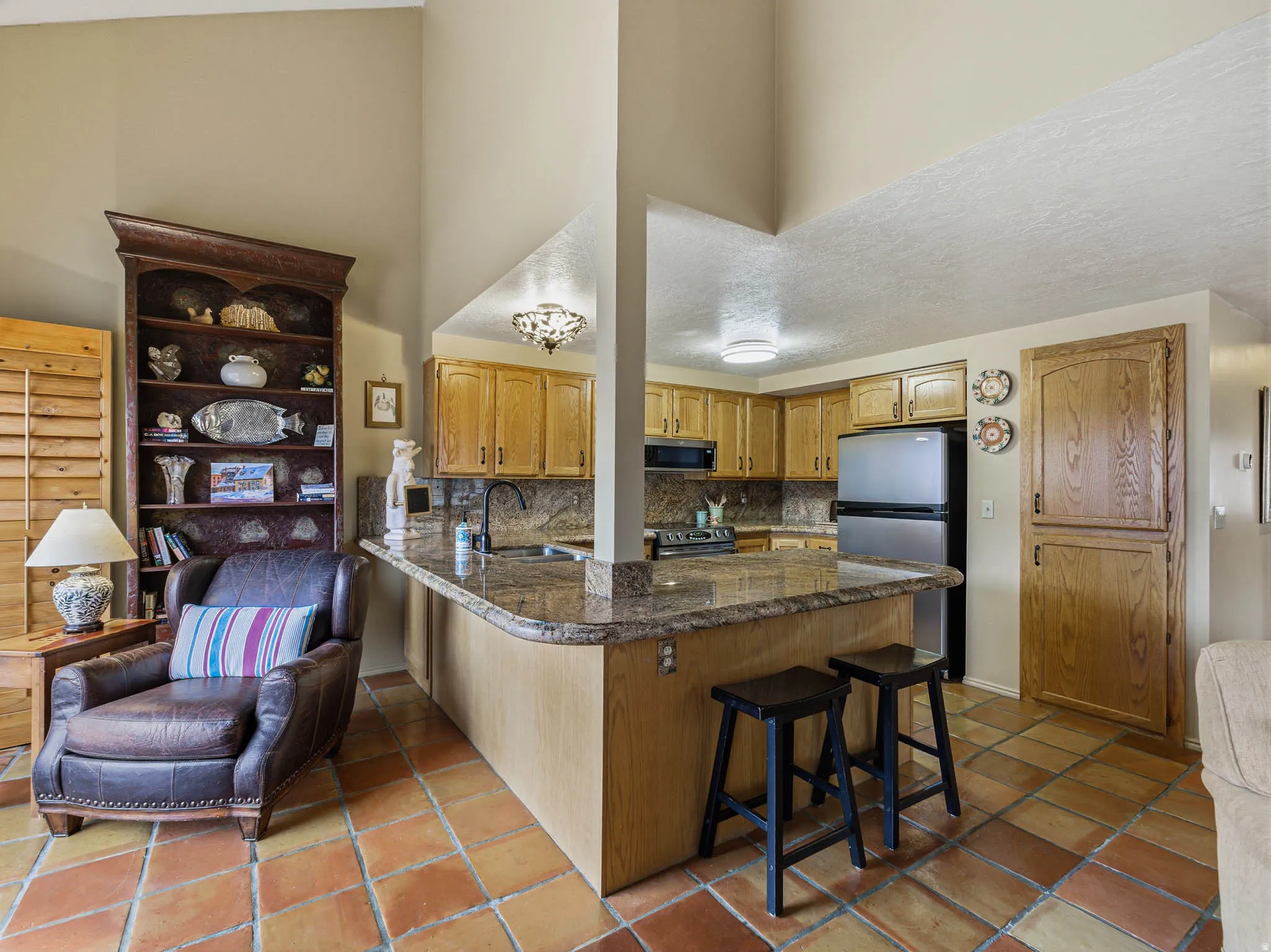 Kitchen with a breakfast bar, a peninsula, stainless steel appliances, decorative backsplash, and a high textured ceiling