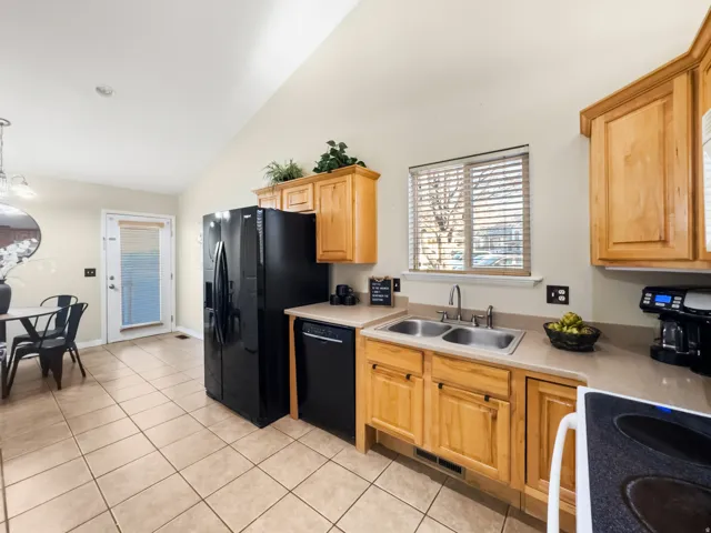 Kitchen featuring black appliances, light countertops, lofted ceiling, light wood finish cabinetry, and light tile patterned floors