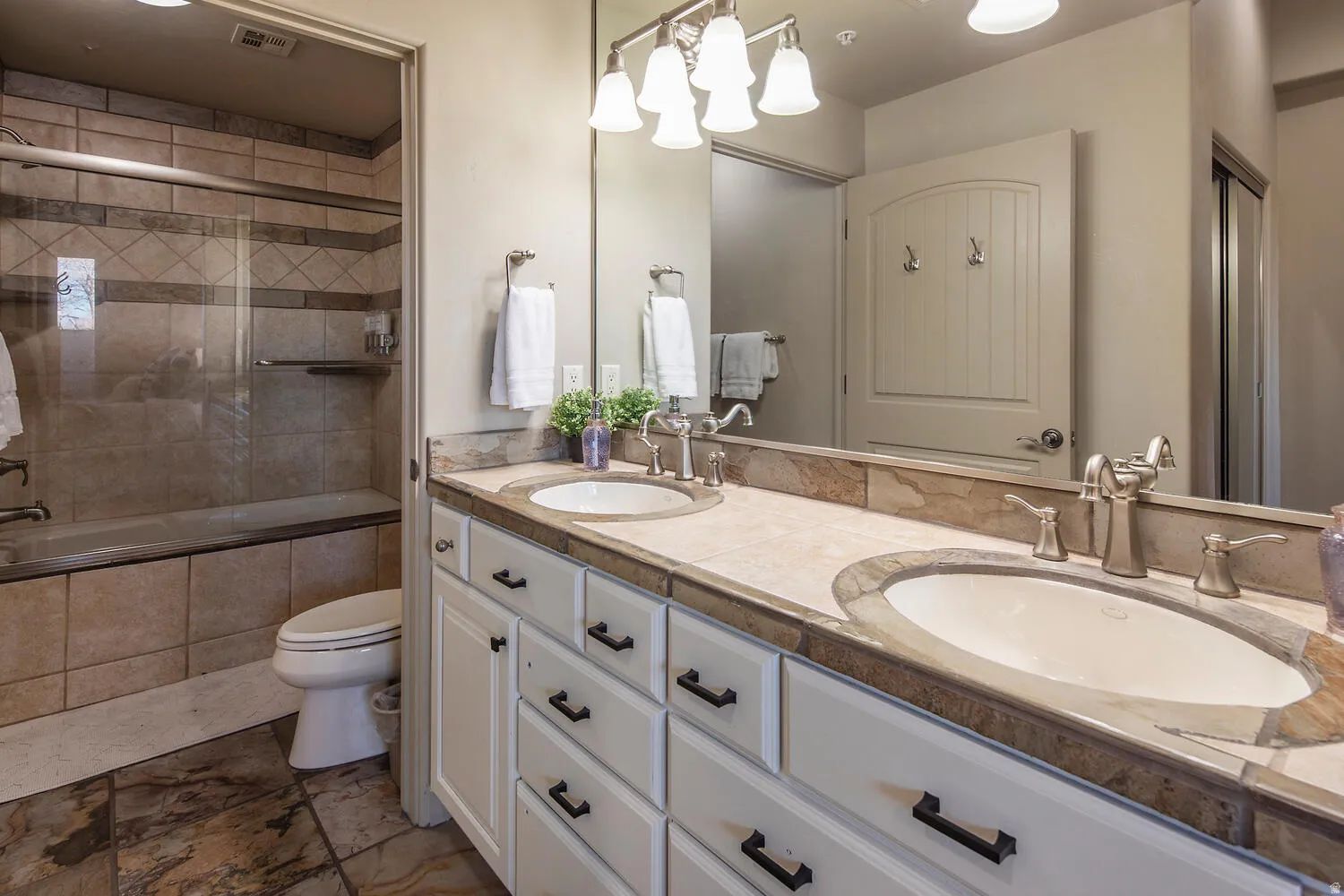 Bathroom with double vanity, tiled shower / bath, and stone finish flooring