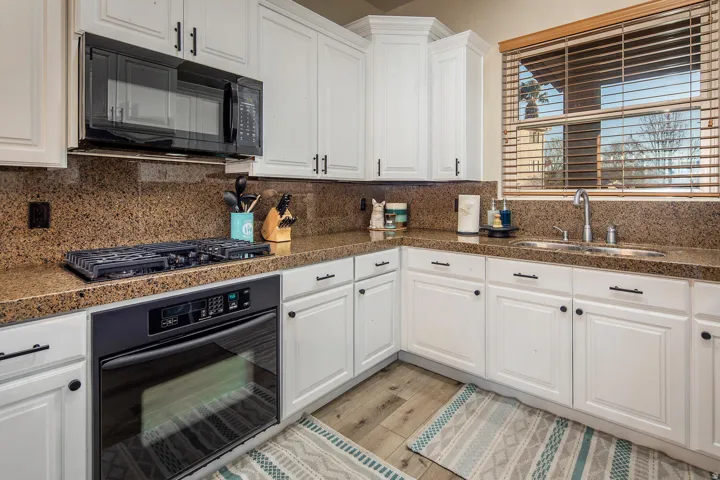 Kitchen featuring black appliances, white cabinetry, tile counters, and light wood finished floors