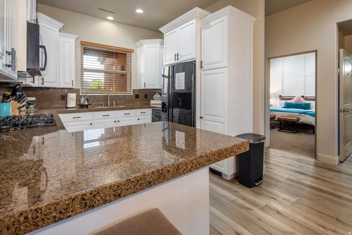 Kitchen with white cabinets, light wood-style floors, black appliances, a peninsula, and backsplash