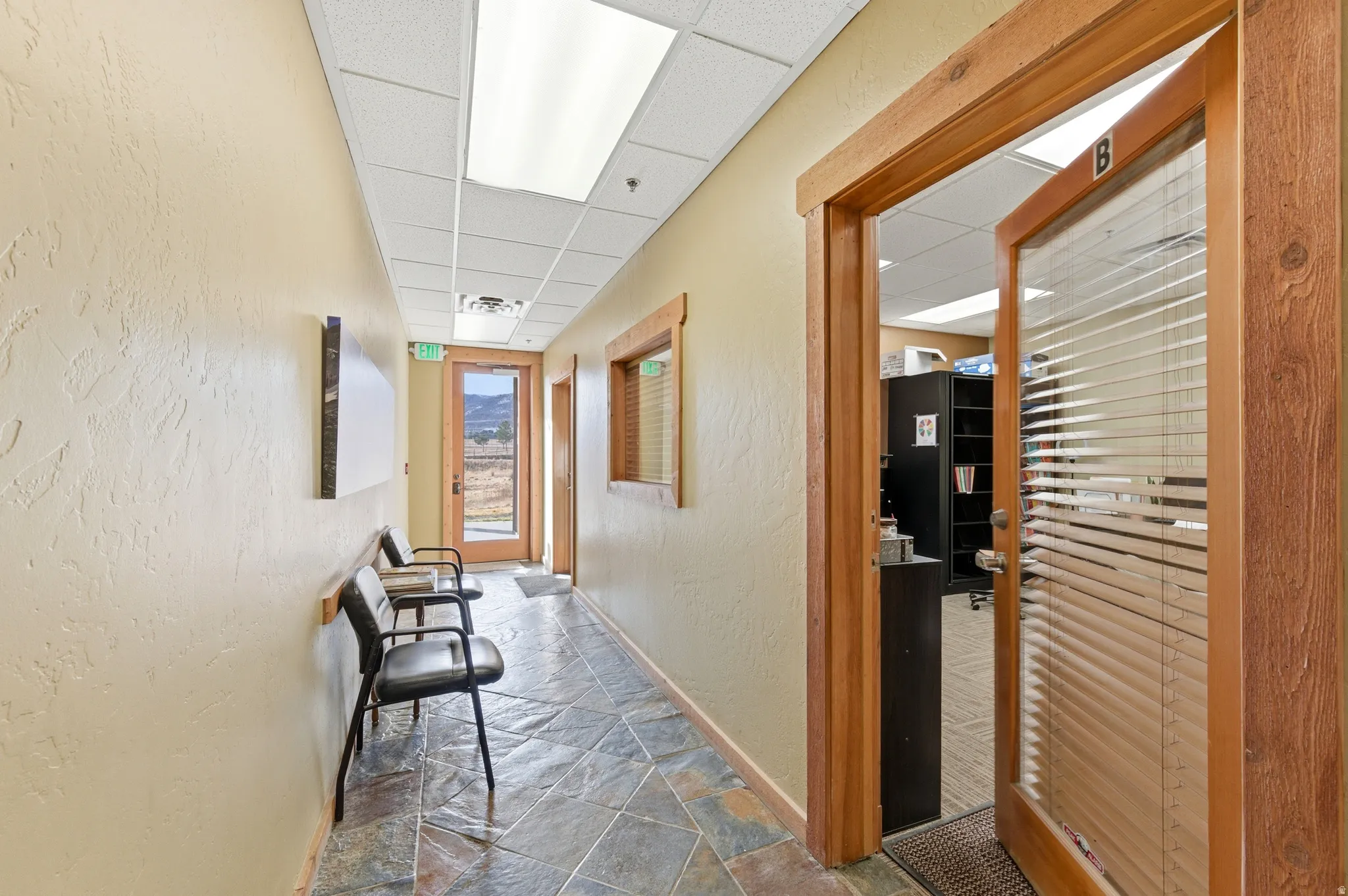 Corridor featuring a textured wall, stone tile floors, and a paneled ceiling