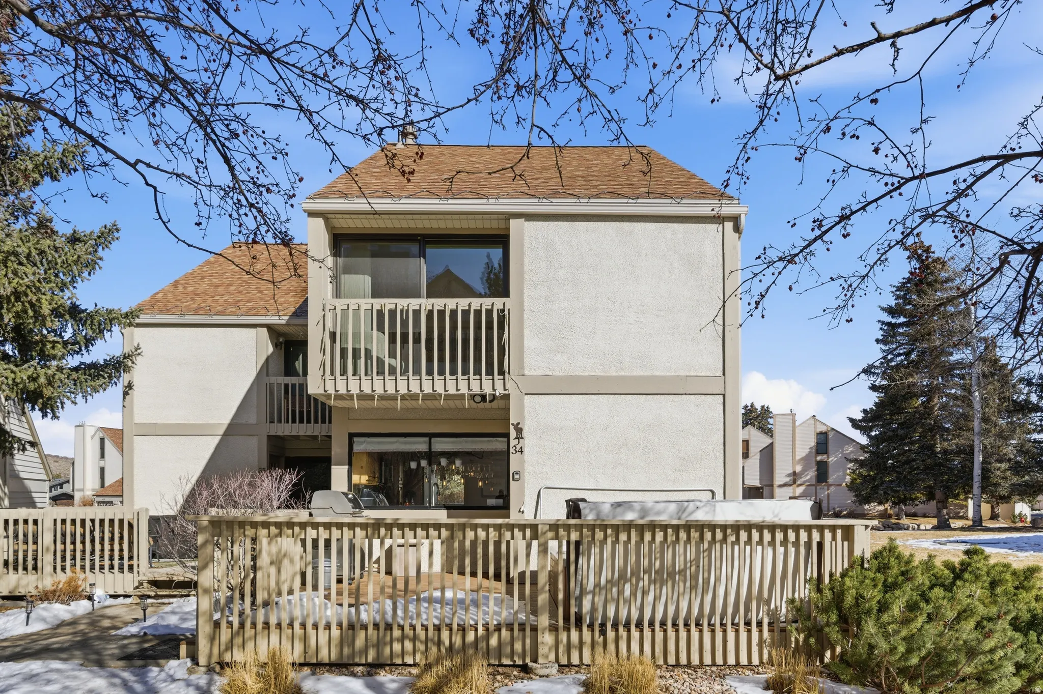 Rear view of house with stucco siding, a balcony, and roof with shingles