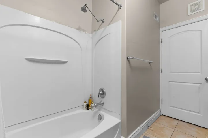 Full bathroom with washtub / shower combination and light tile patterned floors