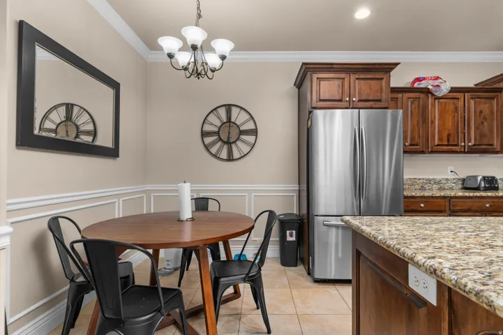 Dining room with hanging lights, crown molding, wainscoting, a decorative wall, and light tile patterned floors