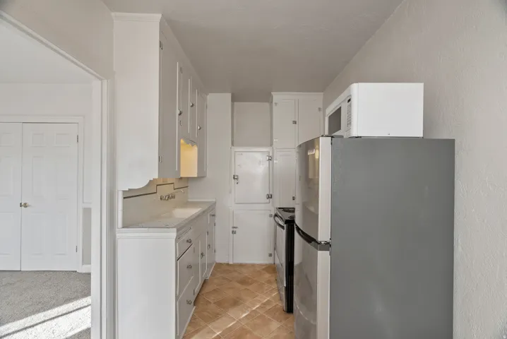 Kitchen featuring stainless steel appliances, light countertops, white cabinets, and a textured wall