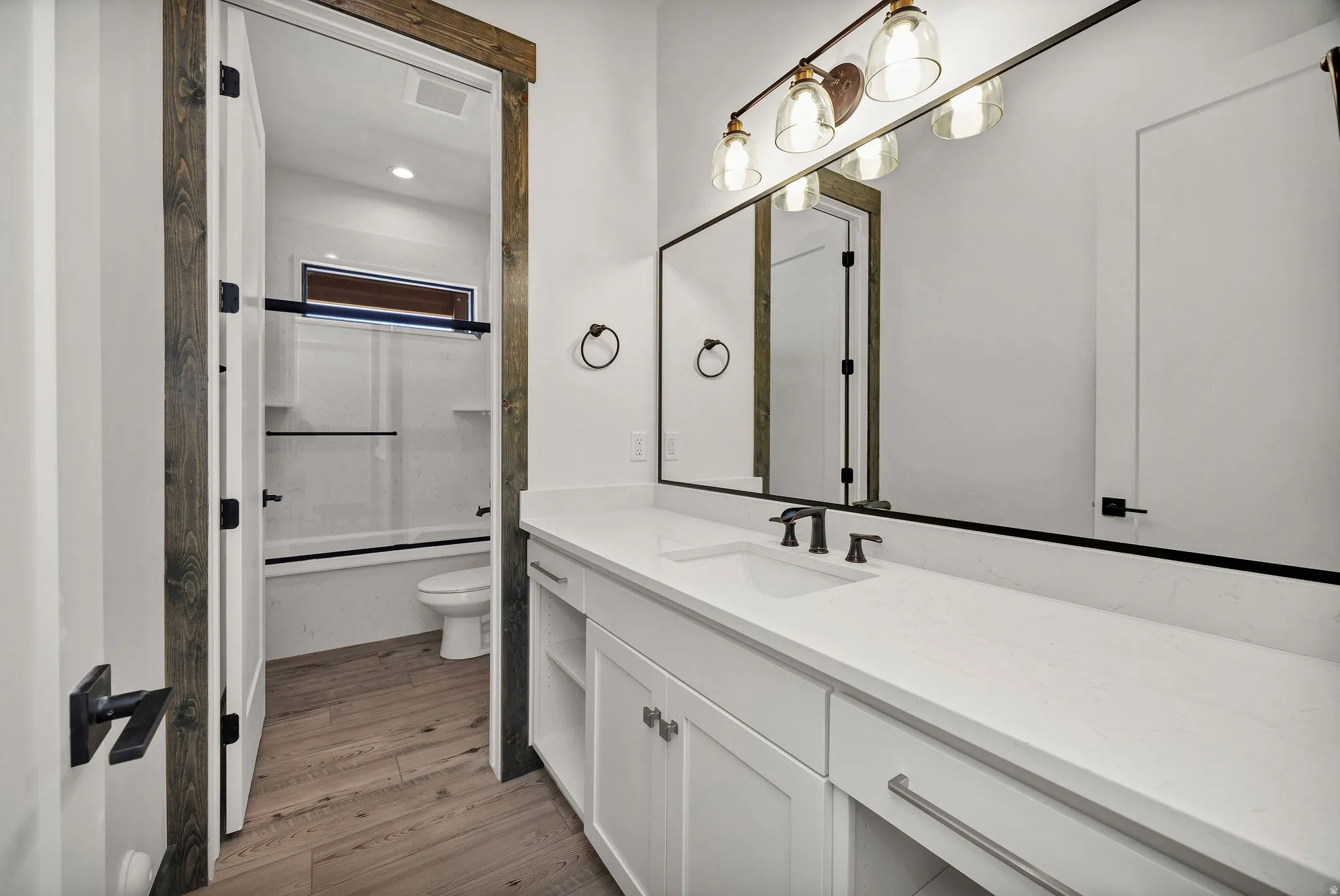 Full bath with vanity, light wood finished floors, bath / shower combo with glass door, and recessed lighting