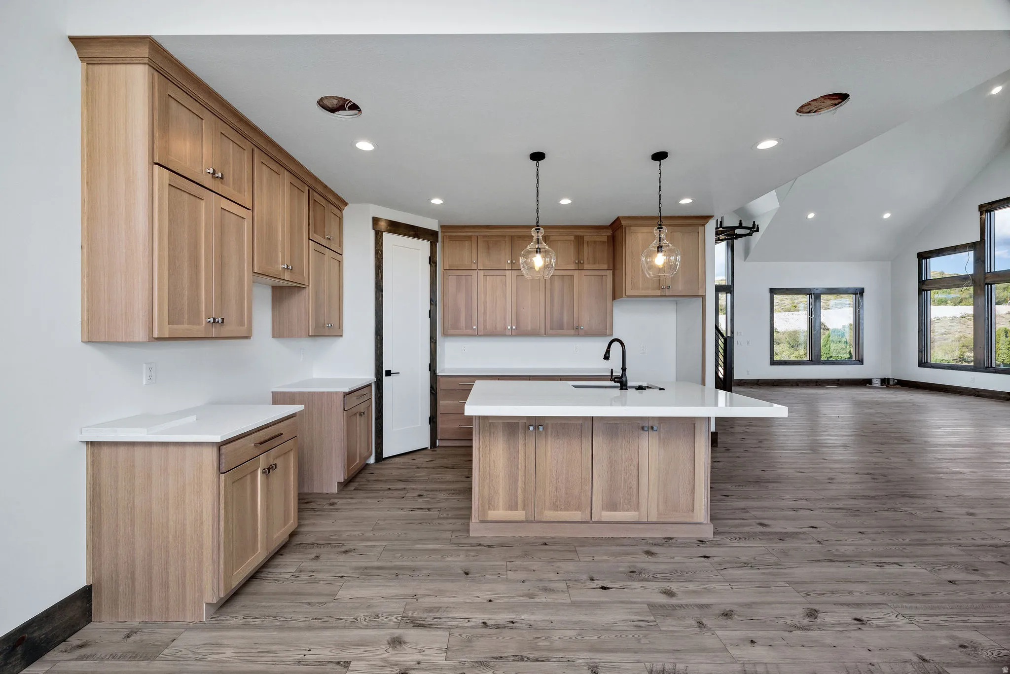 Kitchen featuring vaulted ceiling, a center island with sink, light wood-style flooring, hanging light fixtures, and open floor plan