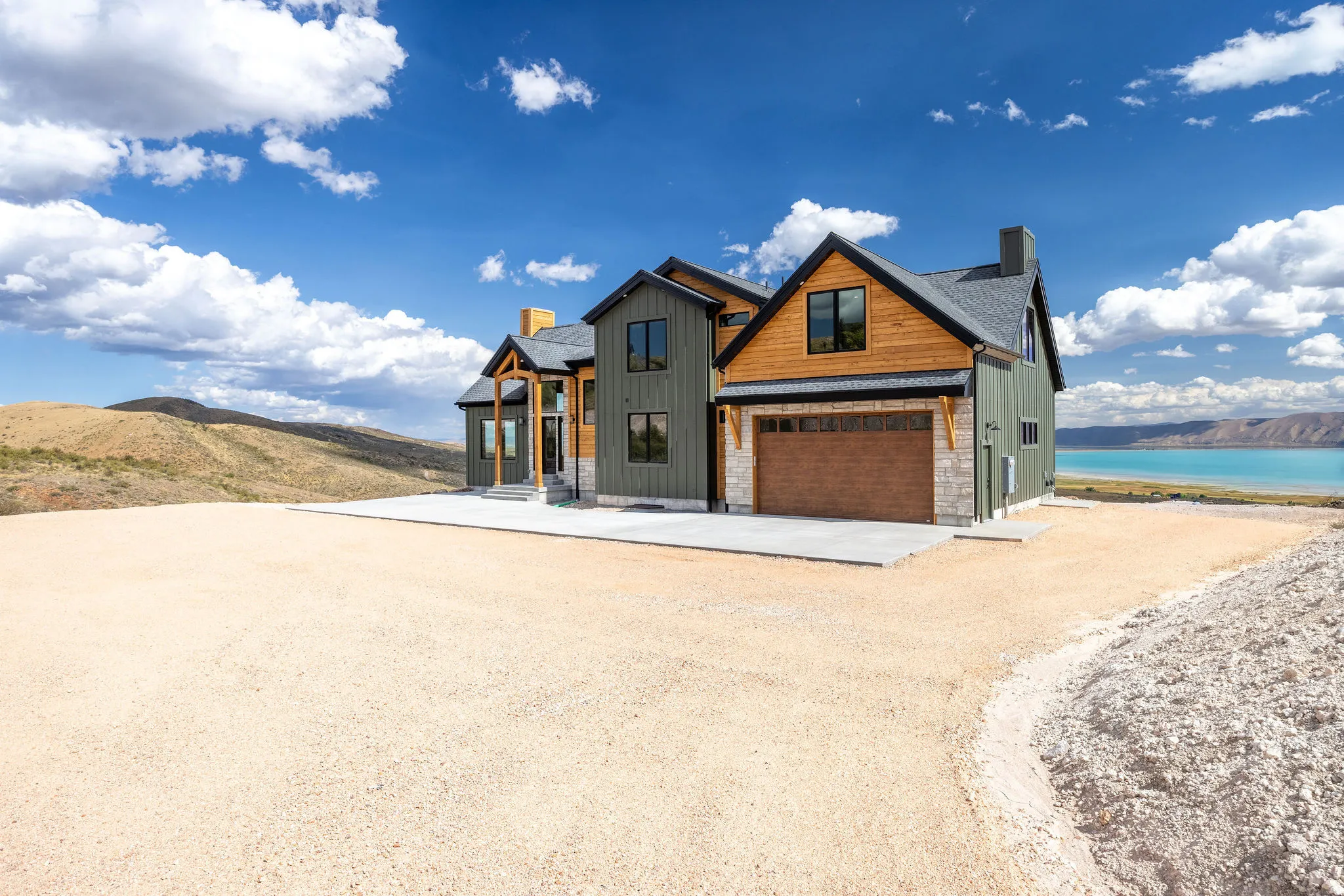 Modern farmhouse style home featuring a chimney, driveway, board and batten siding, stone siding, and a water and mountain view
