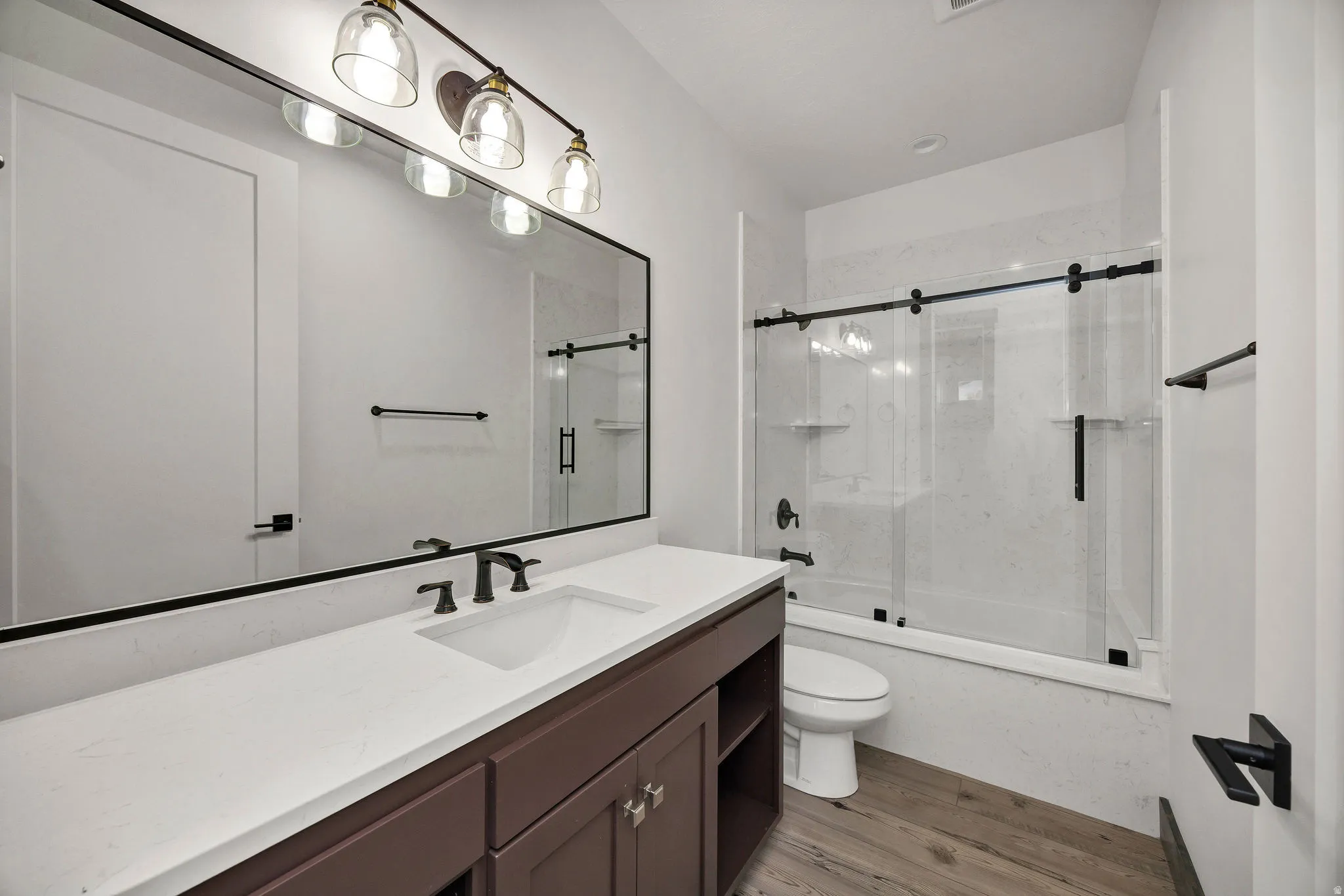 Full bath with shower / bath combination with glass door, vanity, and light wood-style flooring