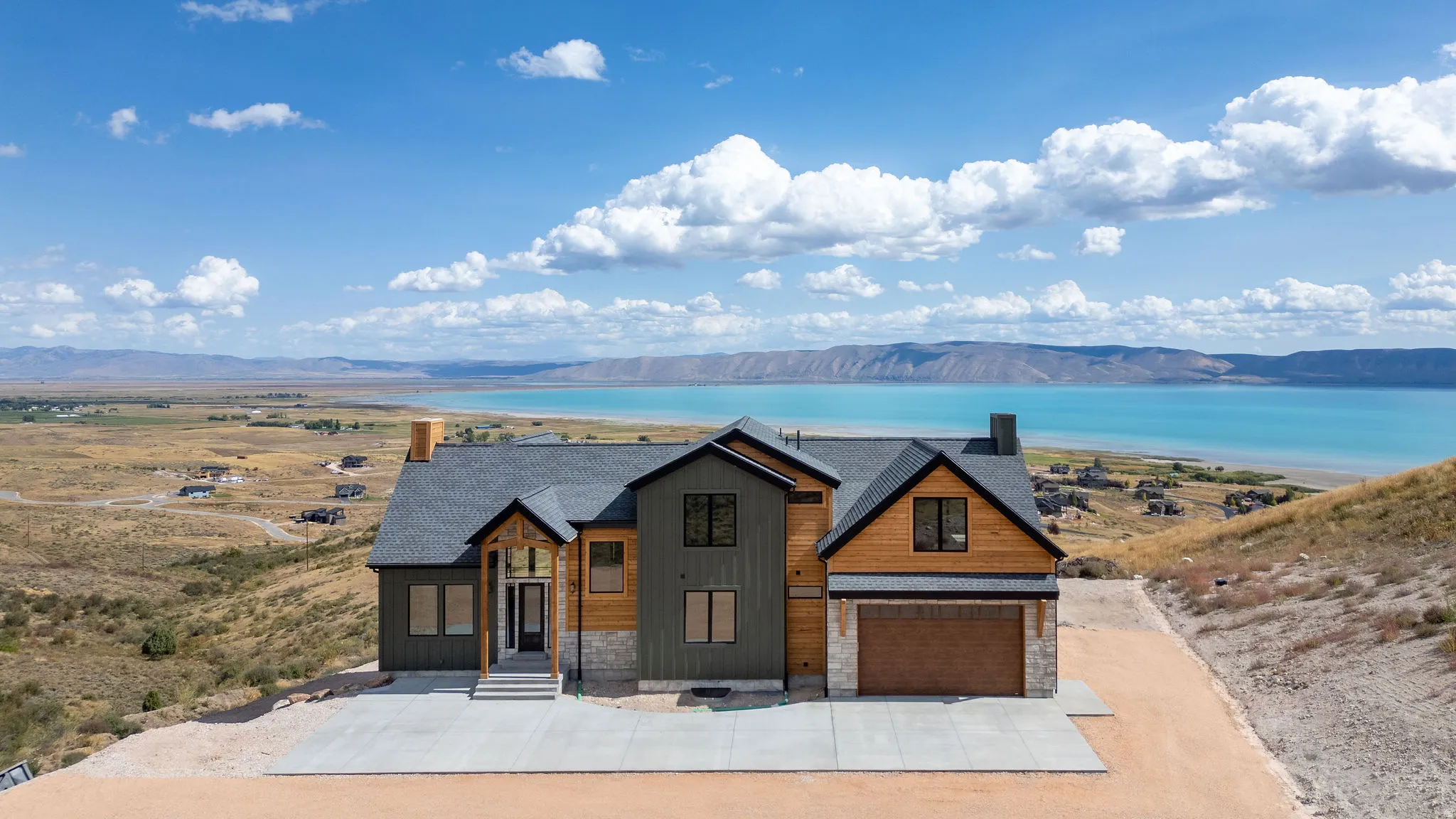 View of front of home featuring stone siding, a garage, driveway, a water and mountain view, and a shingled roof