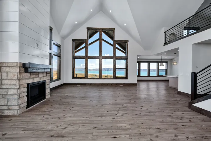 Unfurnished living room featuring a high ceiling, a stone fireplace, wood finished floors, and recessed lighting