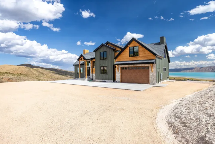 Modern farmhouse style home featuring a chimney, driveway, board and batten siding, stone siding, and a water and mountain view
