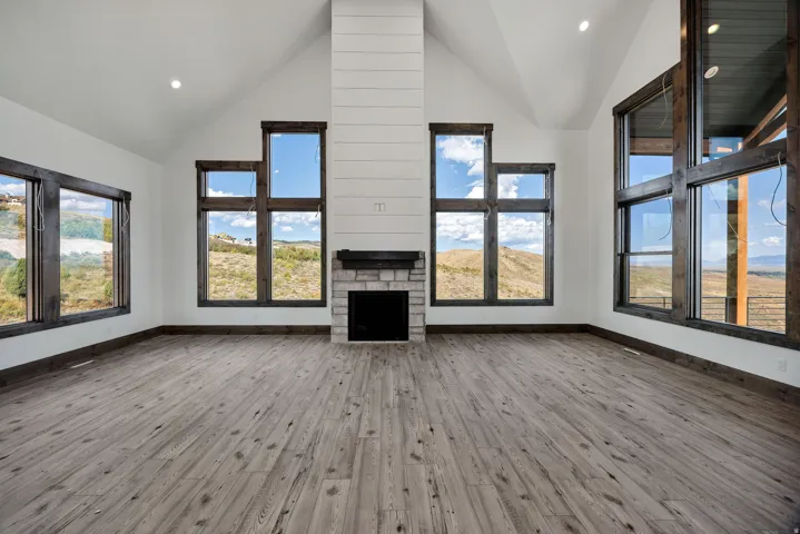 Unfurnished living room with a high ceiling, a stone fireplace, light wood-type flooring, and recessed lighting