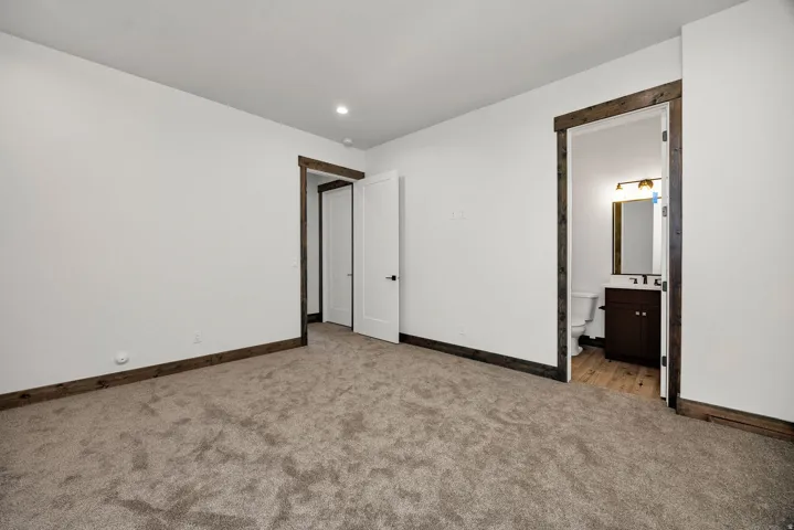 Unfurnished bedroom with light carpet, ensuite bath, and recessed lighting