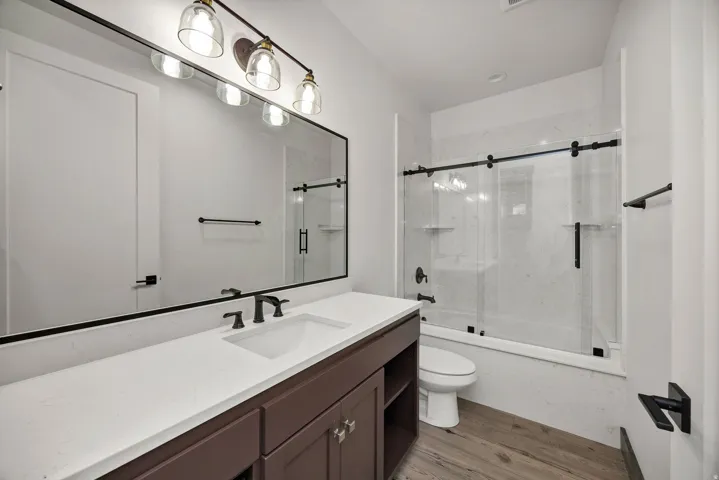 Full bath with shower / bath combination with glass door, vanity, and light wood-style flooring