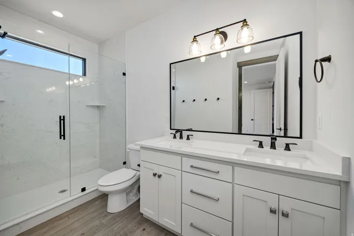 Full bath with double vanity, a marble finish shower, light wood finished floors, and recessed lighting