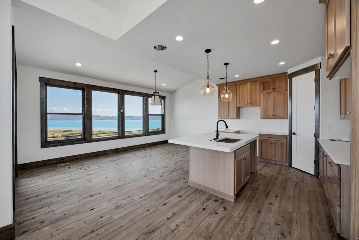Kitchen featuring lofted ceiling, hanging light fixtures, a center island with sink, wood finish cabinetry, and light wood finished floors