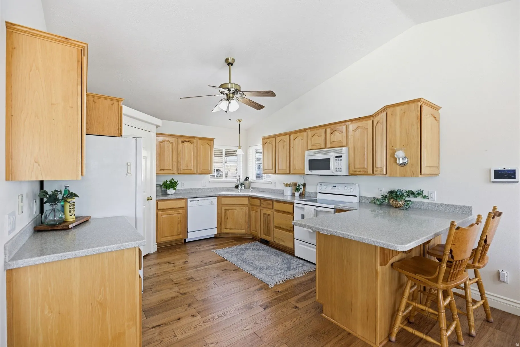 Kitchen featuring dark wood-style flooring, light stone countertops, white appliances, vaulted ceiling, and a peninsula