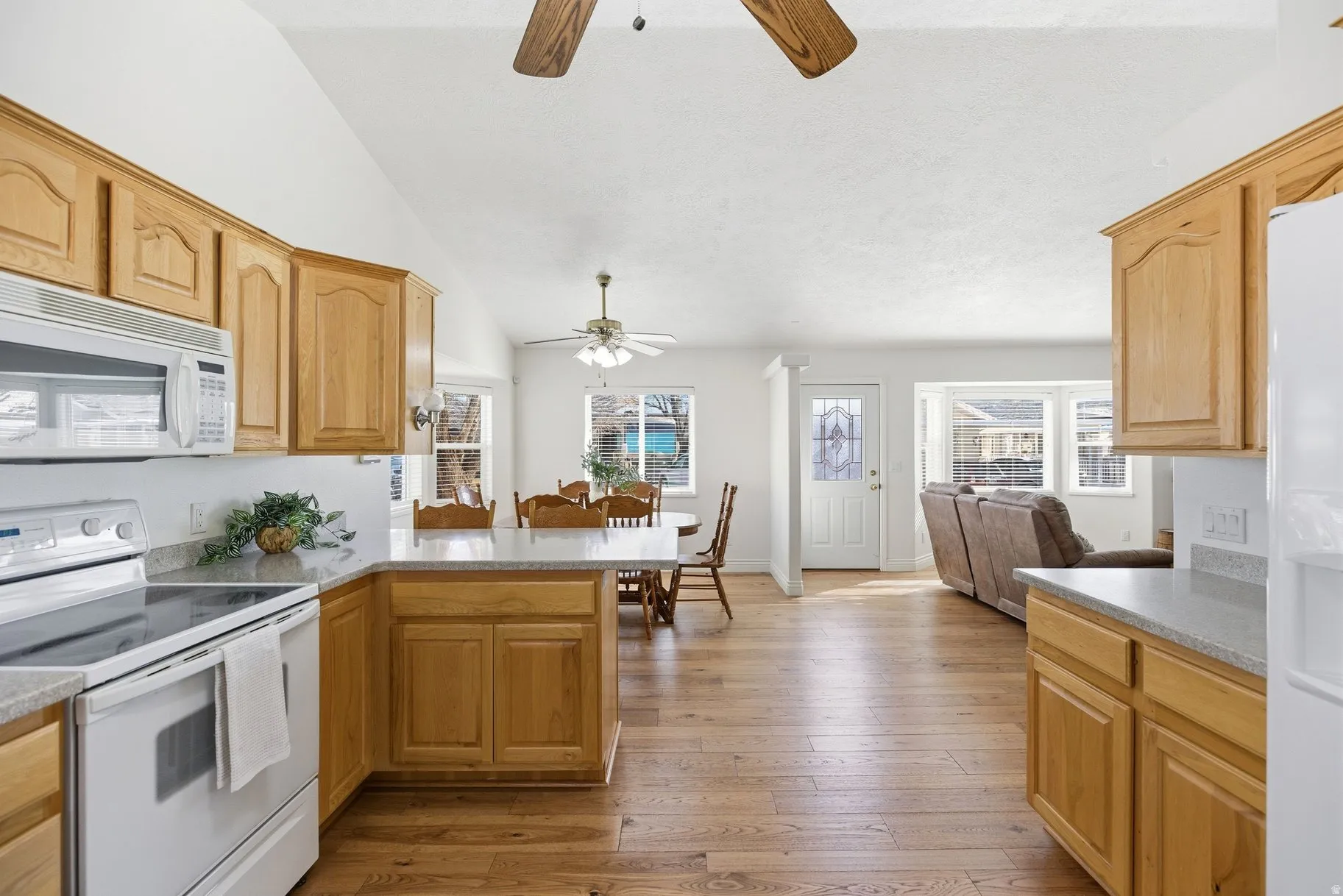 Kitchen featuring white appliances, light wood finished floors, open floor plan, lofted ceiling, and a peninsula