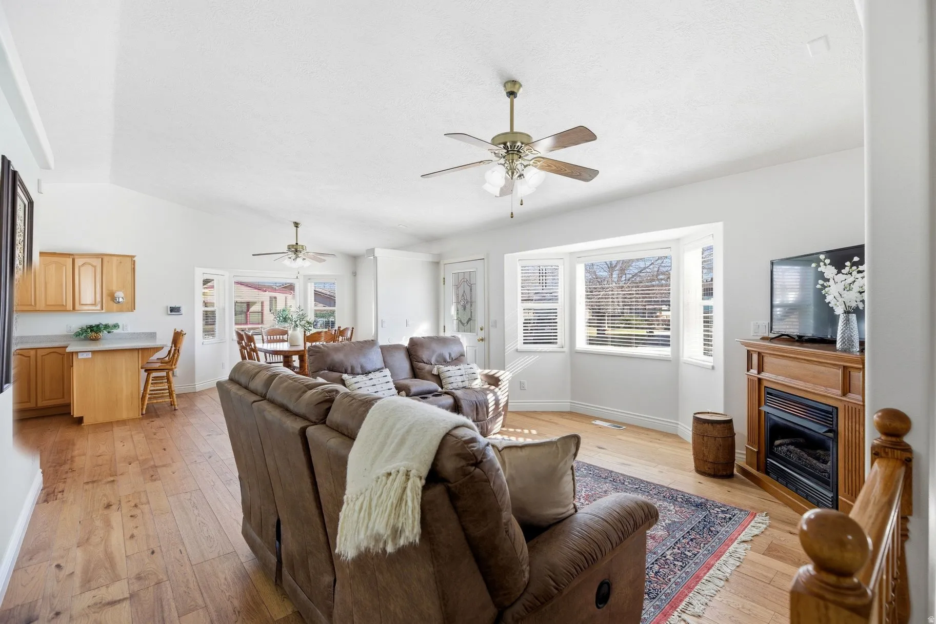 Living room featuring light wood-style flooring, a fireplace, lofted ceiling, and a ceiling fan