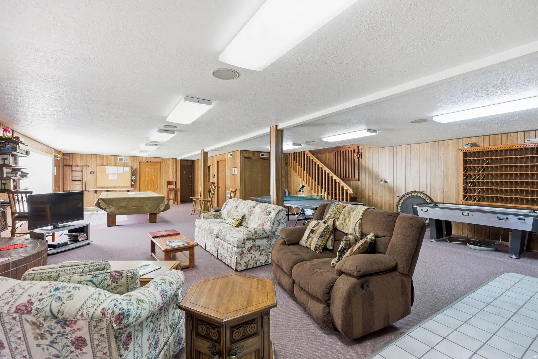 Living room with a textured ceiling, wood walls, pool table, and carpet flooring