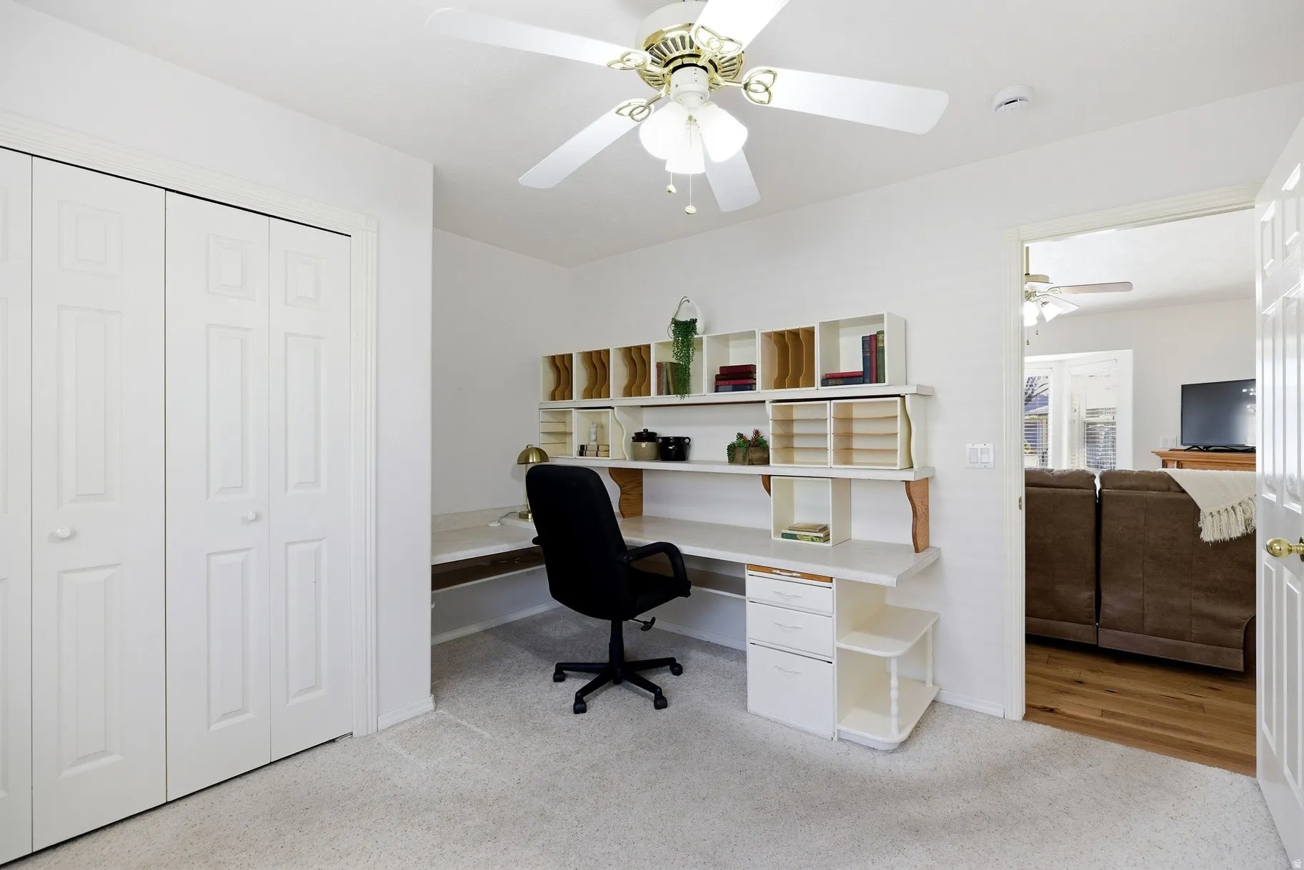 Home office with light carpet, built in desk, and ceiling fan