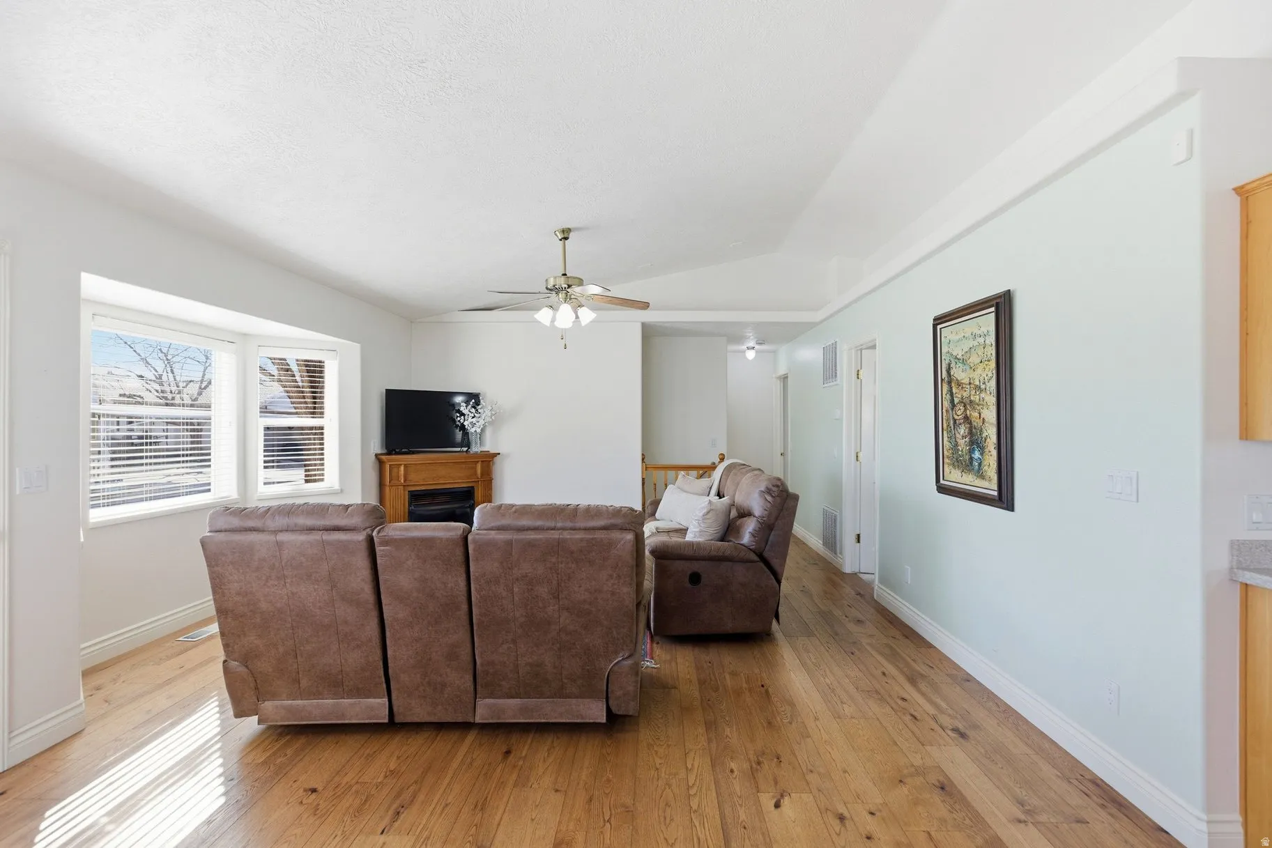 Living room with light wood finished floors, a ceiling fan, a fireplace, and vaulted ceiling