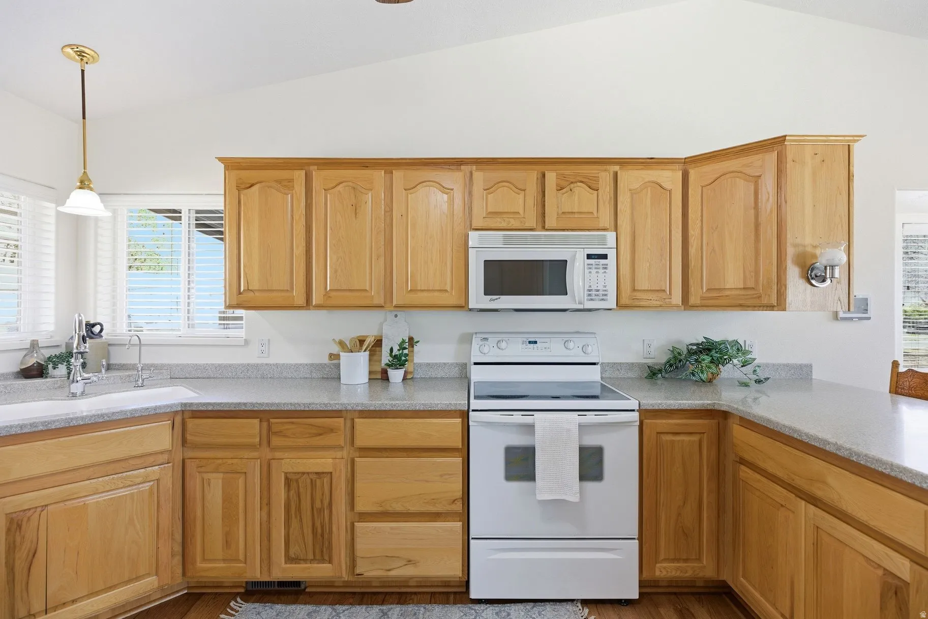 Kitchen with white appliances, hanging light fixtures, lofted ceiling, light stone countertops, and light wood-type flooring