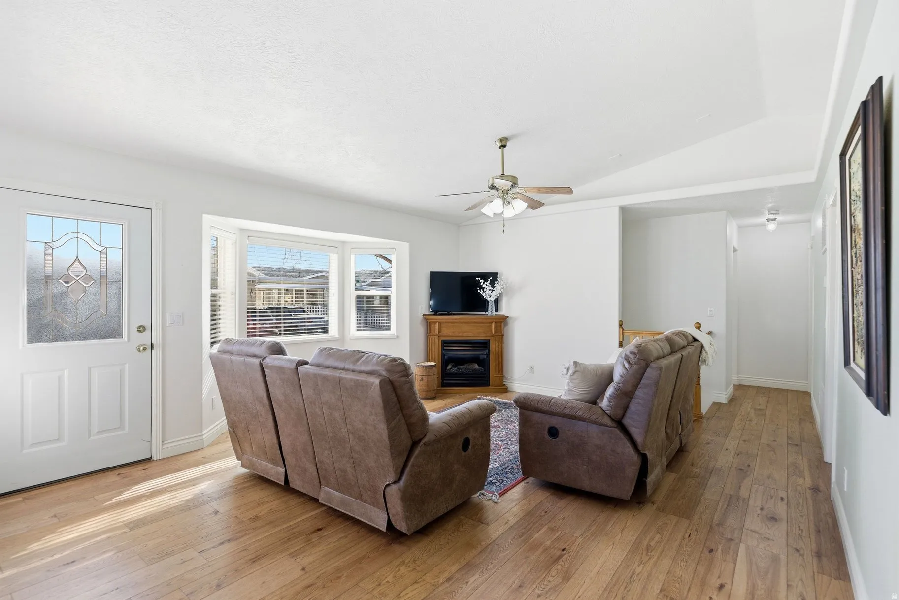 Living room with light wood-style floors, lofted ceiling, ceiling fan, and a glass covered fireplace