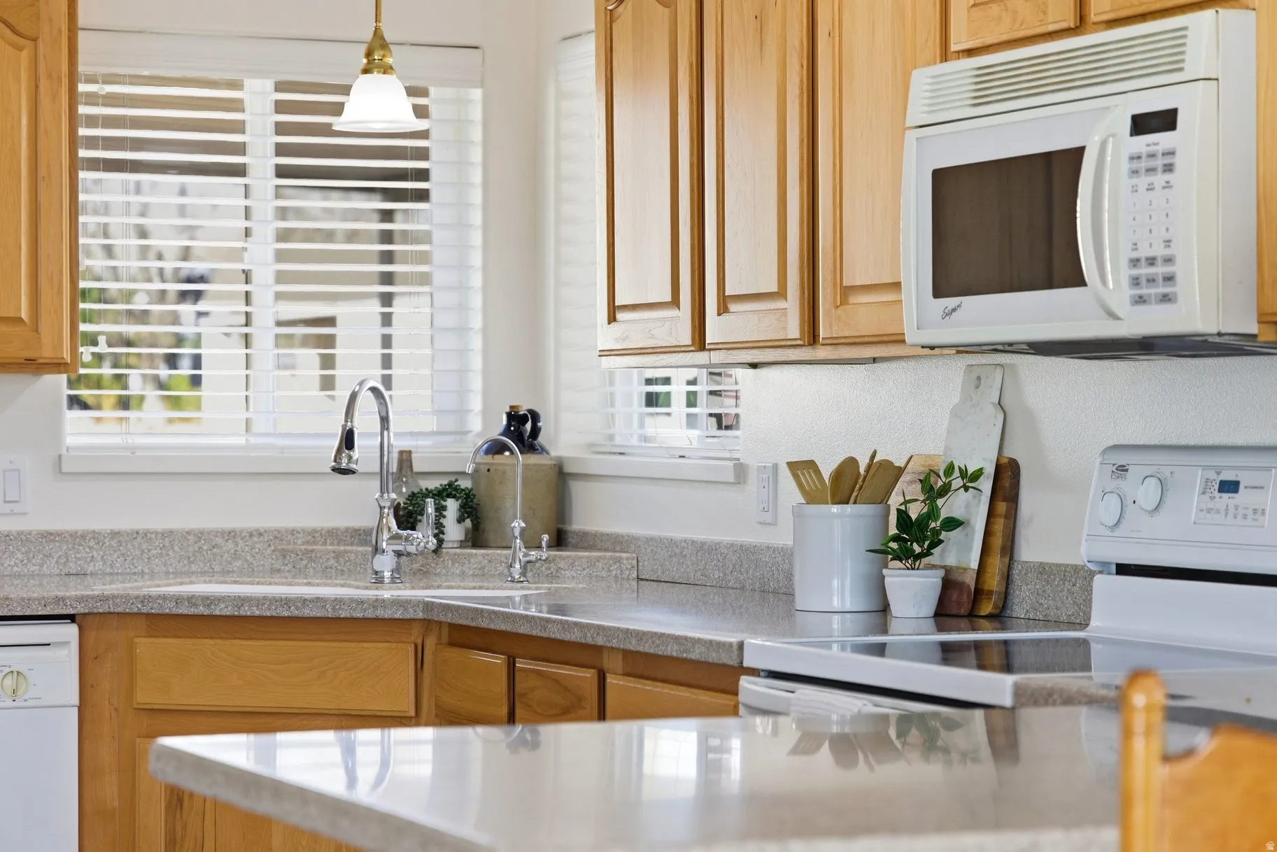 Kitchen featuring white appliances, pendant lighting, and light stone countertops