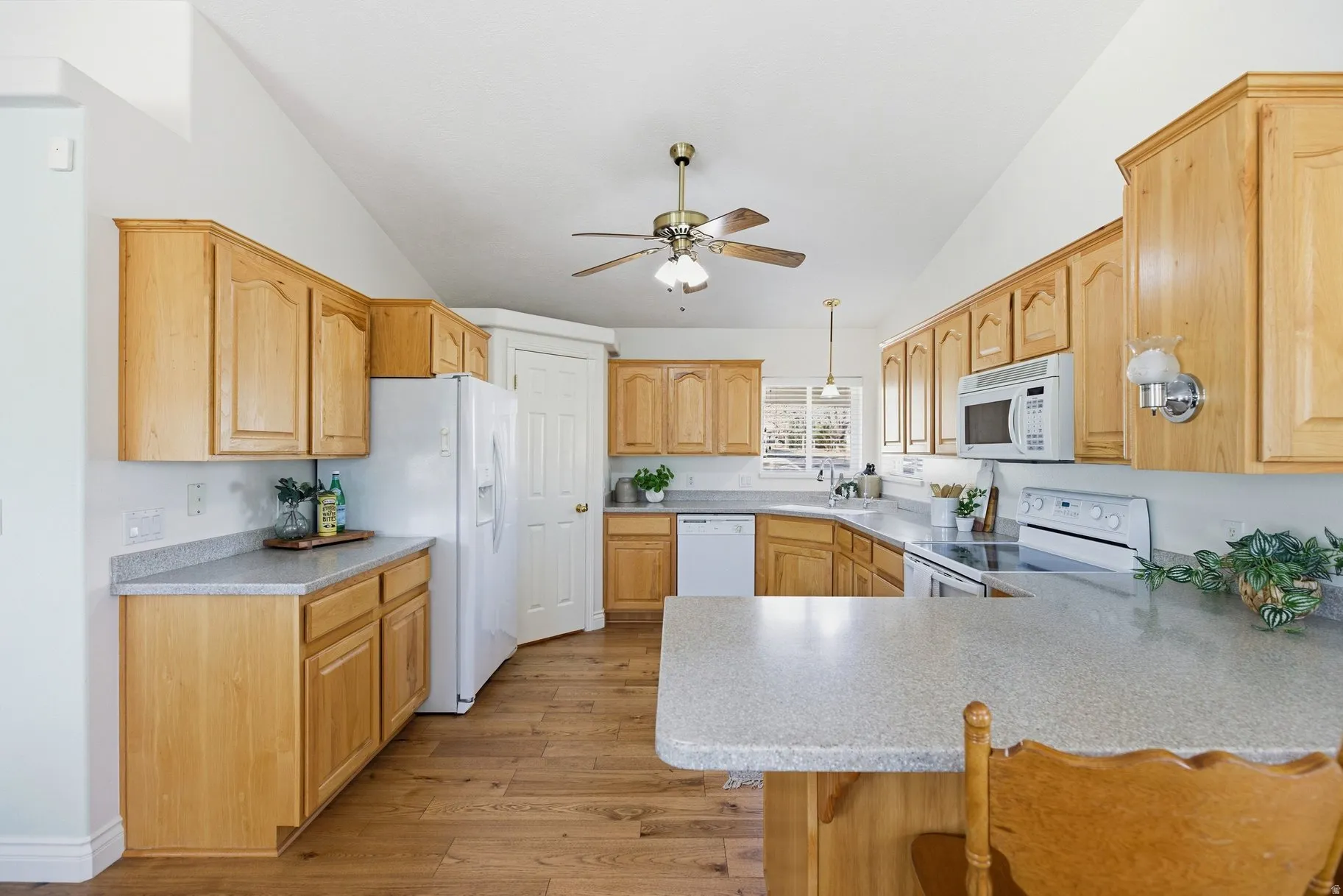Kitchen featuring white appliances, light wood finished floors, lofted ceiling, a ceiling fan, and a peninsula