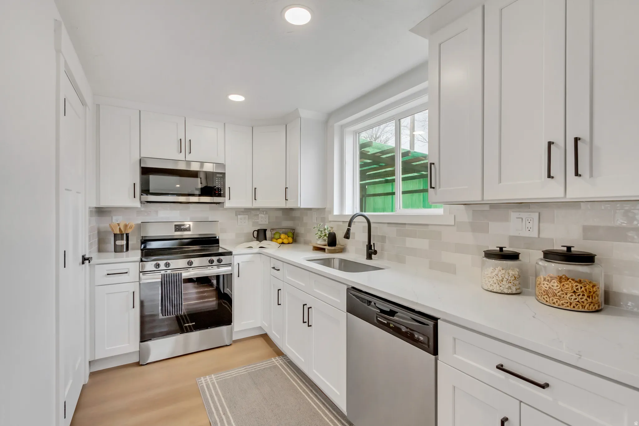 Kitchen with stainless steel appliances, white cabinetry, light stone counters, light wood finished floors, and backsplash