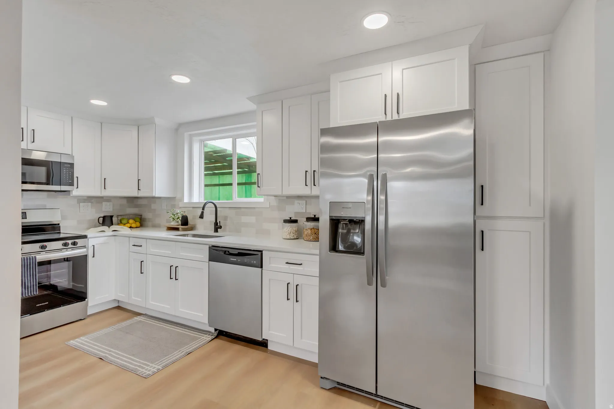 Kitchen featuring stainless steel appliances, white cabinetry, backsplash, light wood-style floors, and recessed lighting