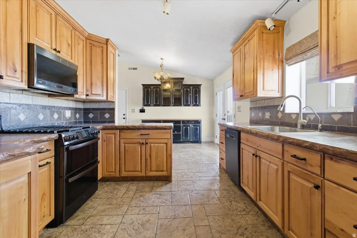 Kitchen featuring range with two ovens, stainless steel microwave, stone tile floors, decorative backsplash, and lofted ceiling