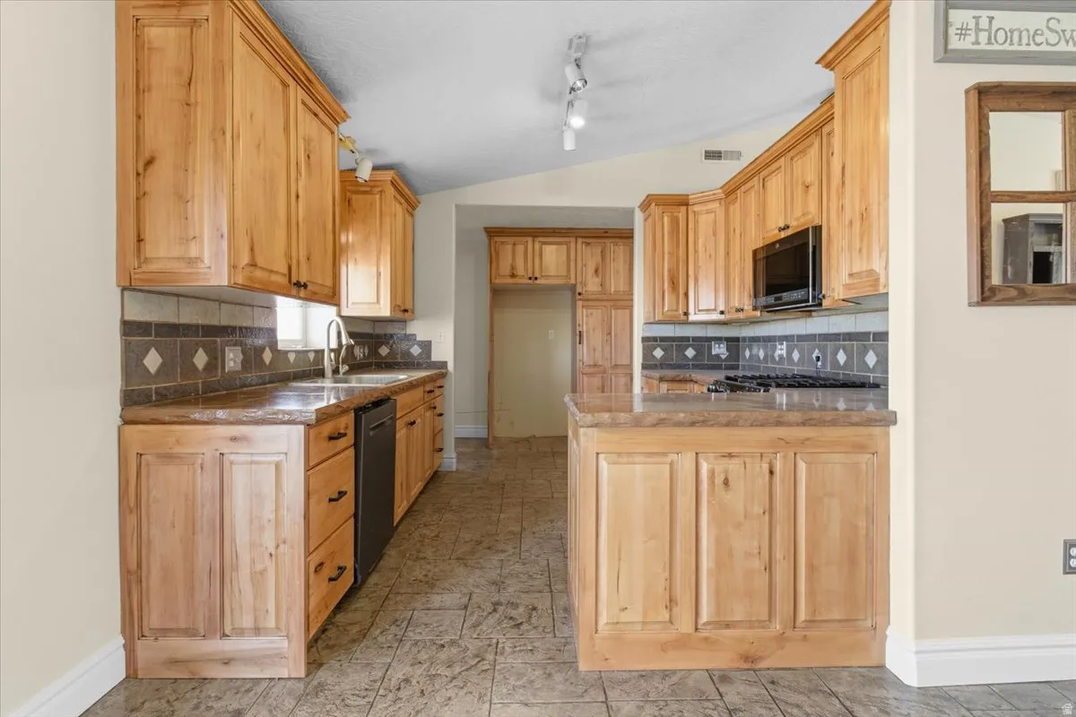 Kitchen with a peninsula, lofted ceiling, tasteful backsplash, light wood finish cabinets, and dishwasher