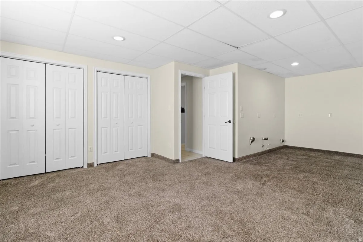 Unfurnished bedroom featuring multiple closets, a drop ceiling, carpet flooring, and recessed lighting