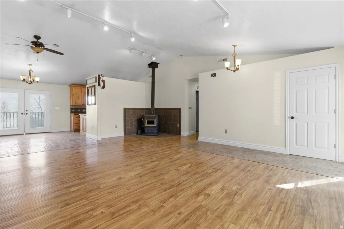 Unfurnished living room featuring a chandelier, ceiling fan, a wood stove, and light wood-style floors