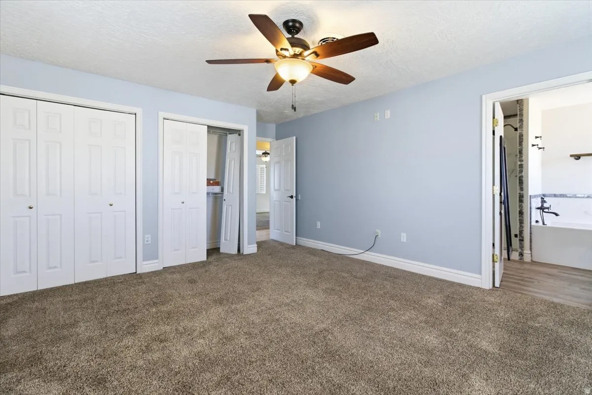 Unfurnished bedroom with multiple closets, carpet flooring, a ceiling fan, and a textured ceiling