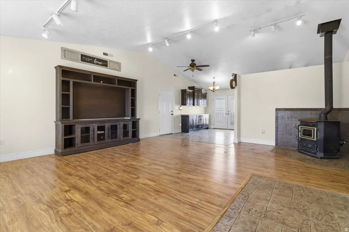 Unfurnished living room with lofted ceiling, ceiling fan, track lighting, light wood-style floors, and a wood stove