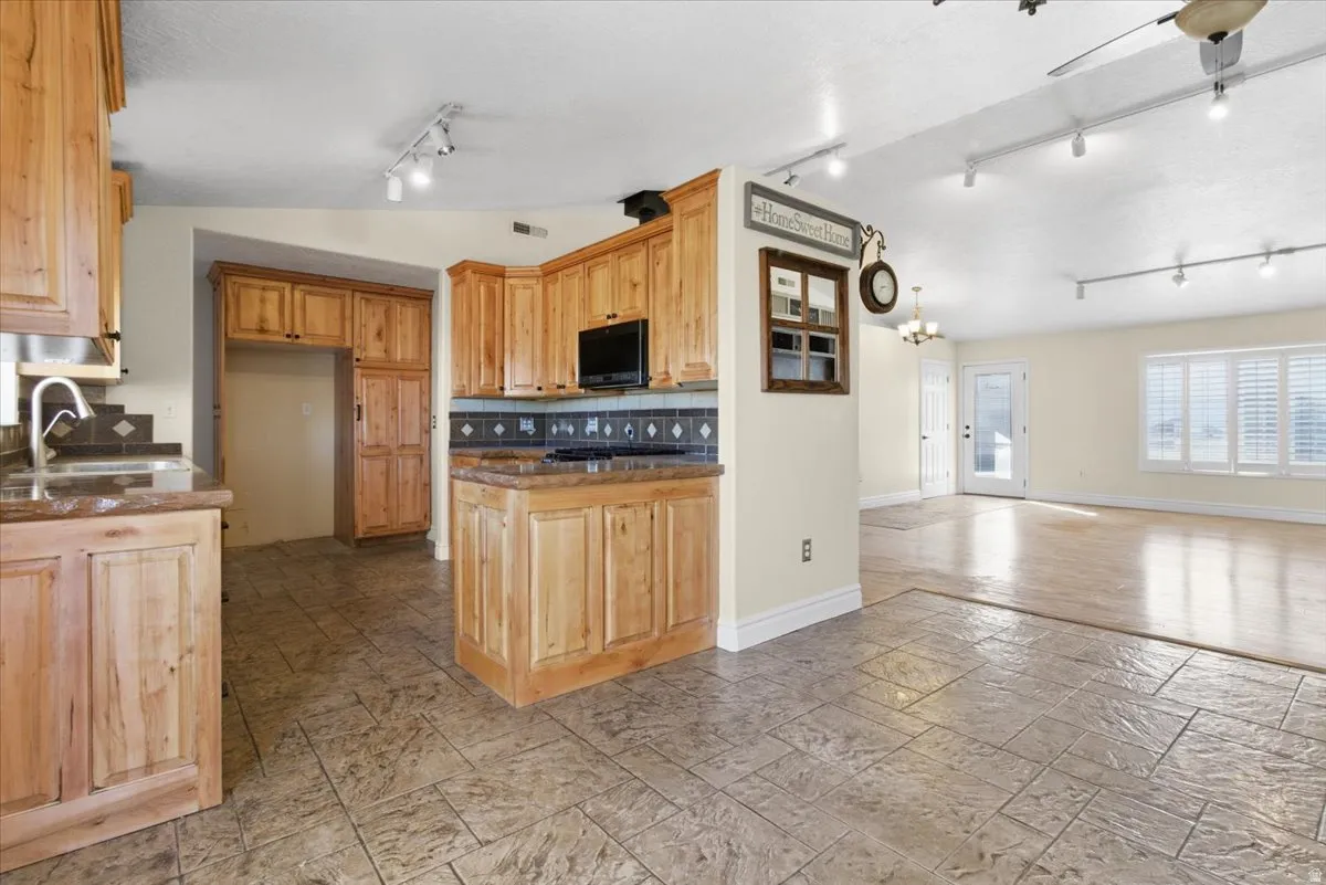 Kitchen featuring open floor plan, stone tile floors, black microwave, a chandelier, and backsplash