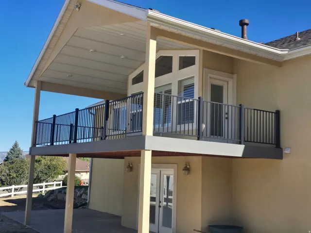 Modern two-story residence featuring a covered upper-deck with black metal railings, substantial support columns, and French doors providing access to the second level