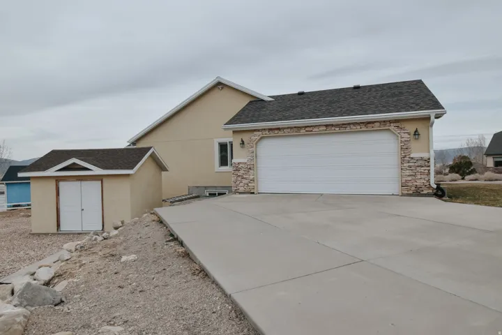 View of front of house with a shingled roof, stucco siding, driveway, stone siding, and an outbuilding