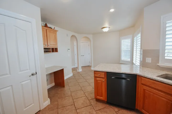 Kitchen with light stone countertops, dishwasher, arched walkways, light tile patterned floors, and a peninsula and dining area