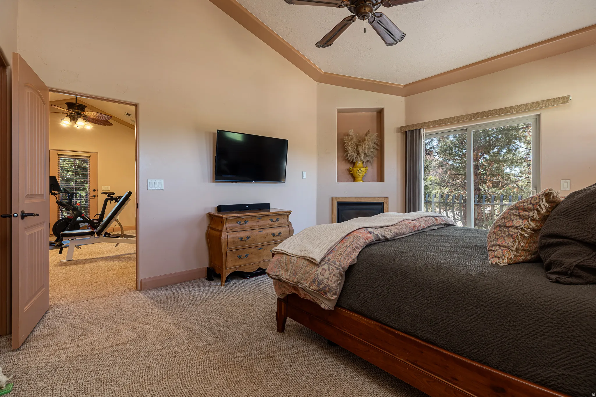 Bedroom featuring light colored carpet, vaulted ceiling, a ceiling fan, access to exterior, and a glass covered fireplace