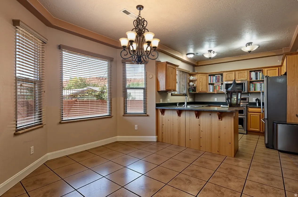 Dining featuring a peninsula, dark countertops, a textured ceiling, suspended lighting, and light tile patterned floors