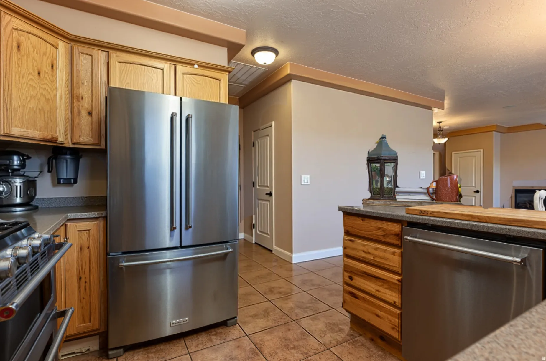 Kitchen featuring stainless steel appliances, dark countertops, light tile patterned flooring, a textured ceiling, and wood finish cabinetry
