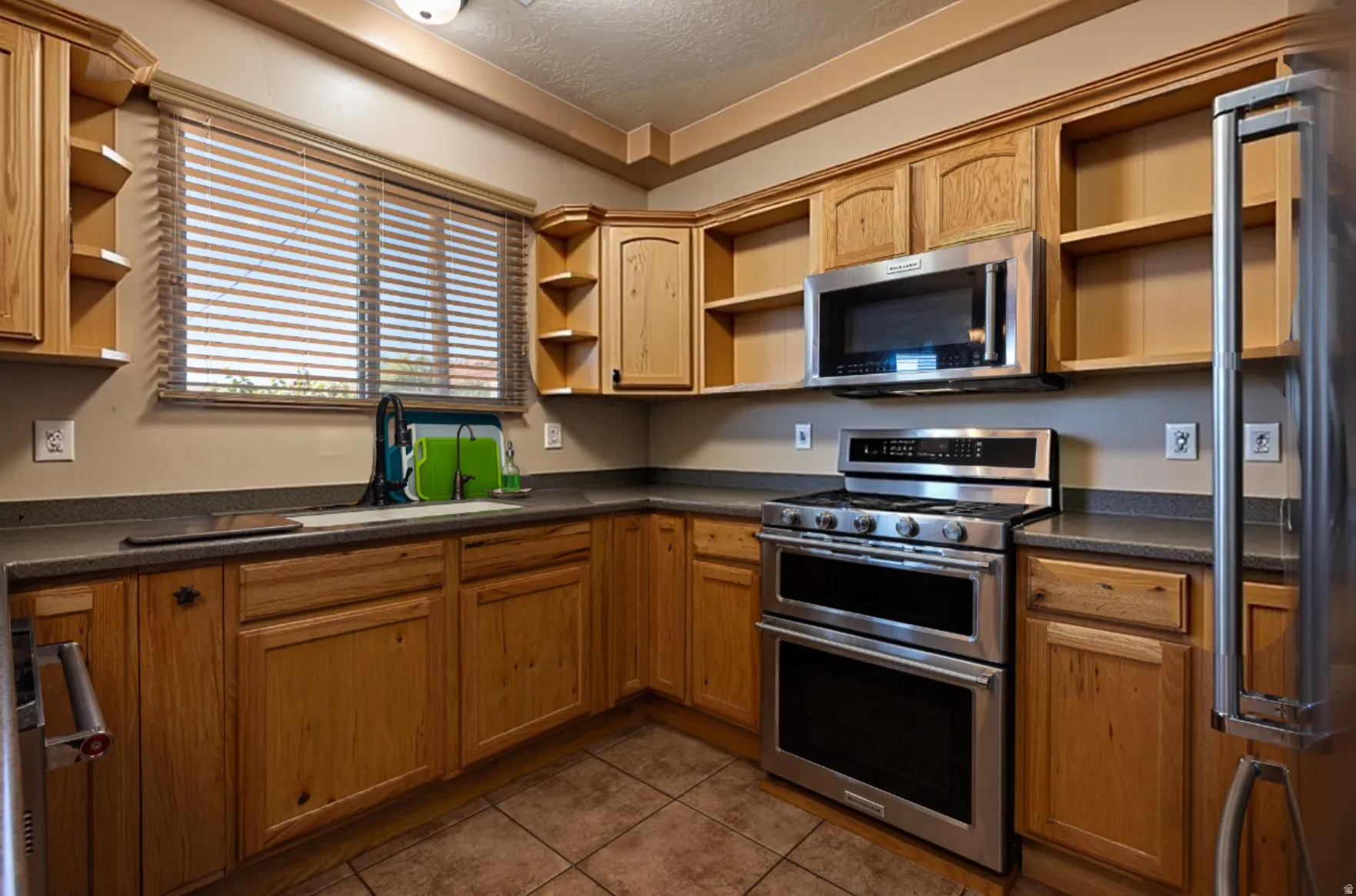 Kitchen featuring open shelves, stainless steel appliances, dark countertops, and a textured ceiling