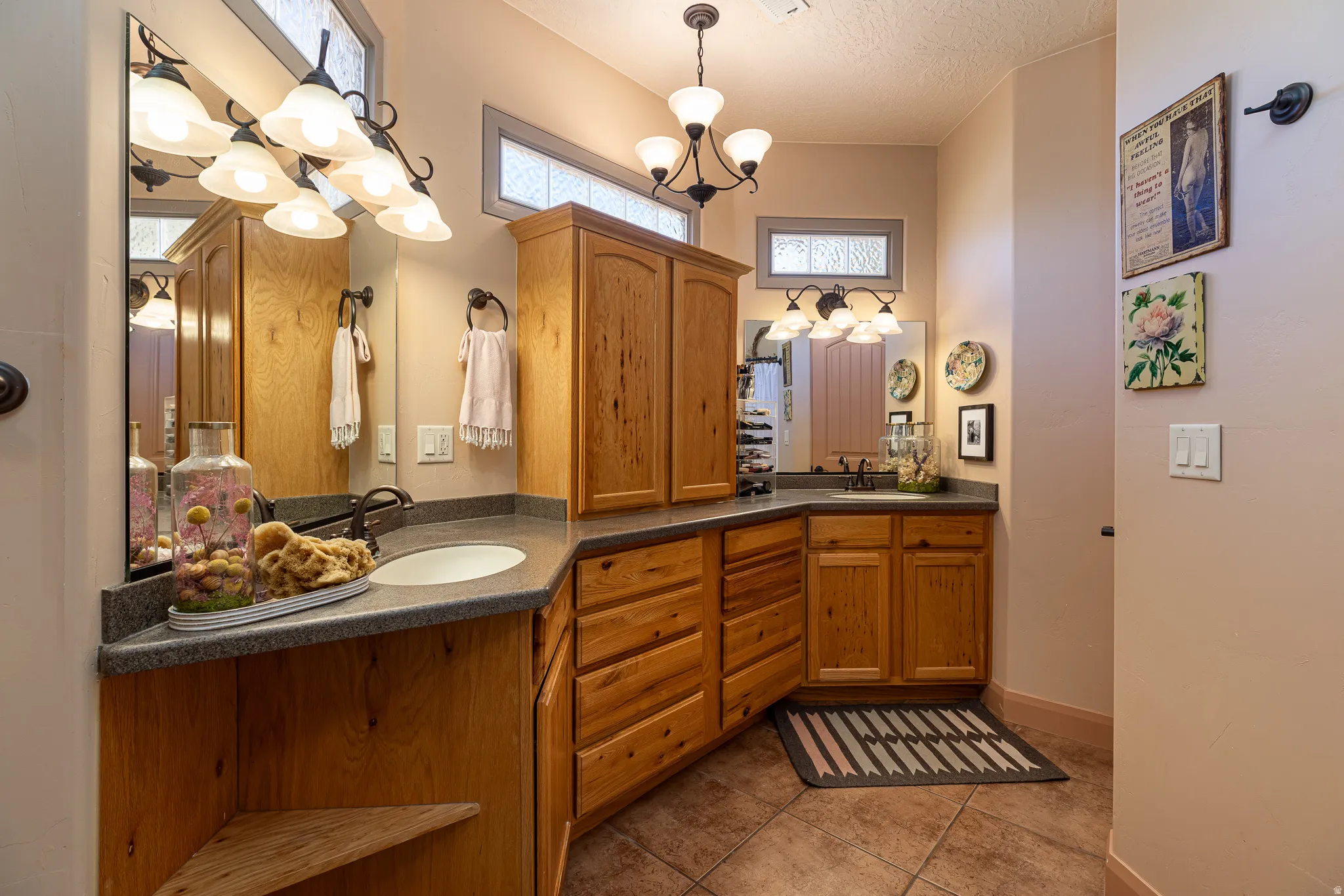 Full bath with double vanity, light tile patterned flooring, hanging lights, and a textured ceiling