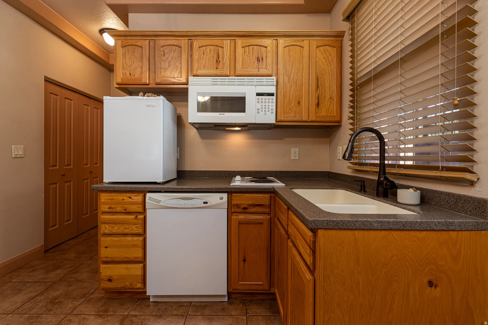 Kitchen with dark countertops, white appliances, wood finish cabinets, and light tile patterned floors
